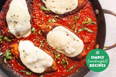 Chicken Parmesan with melted cheese in a skillet with tomato sauce and basil garnish