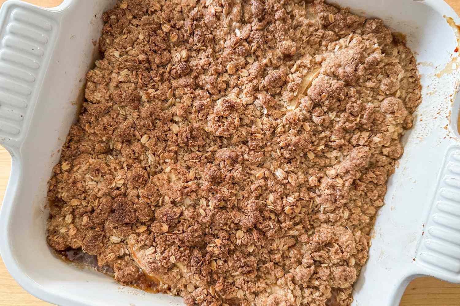 A baked plum crisp in a square baking dish with an oat and cinnamon crumble topping
