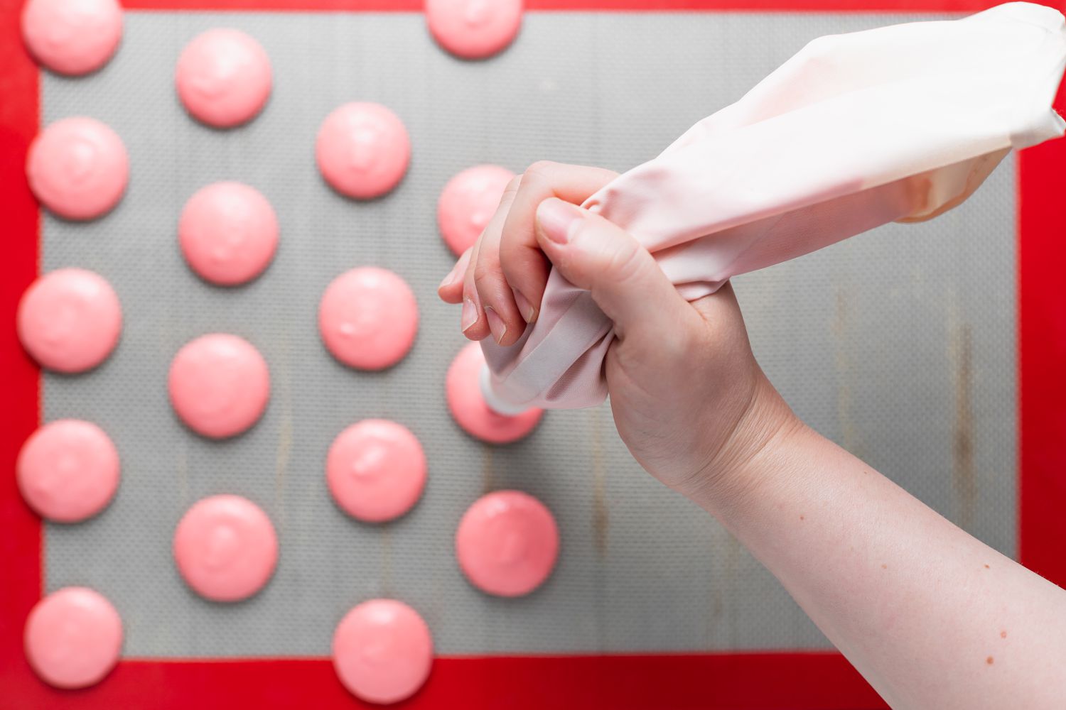 Piping raspberry macarons onto a silicone mat.