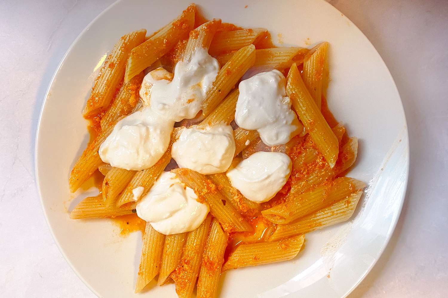 Pasta with a red sauce and dollops of white cheese on a plate