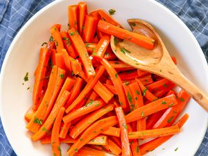 Overhead shot of a white shallow bowl with julienned carrots tossed in herbs and a wooden serving spoon