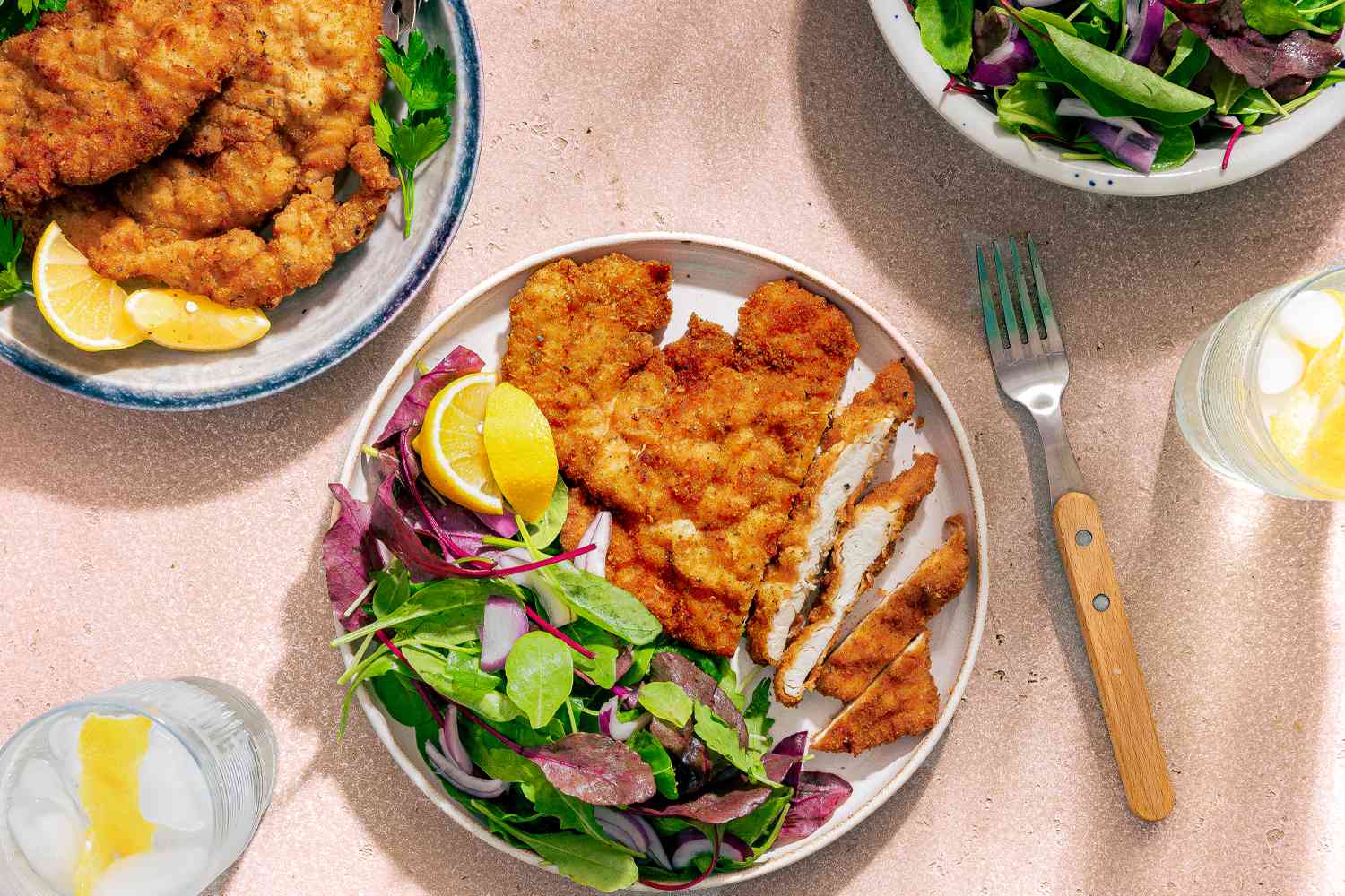 Chicken Romano on a plate with a side salad, fork and glass of ice water with lemon on the side
