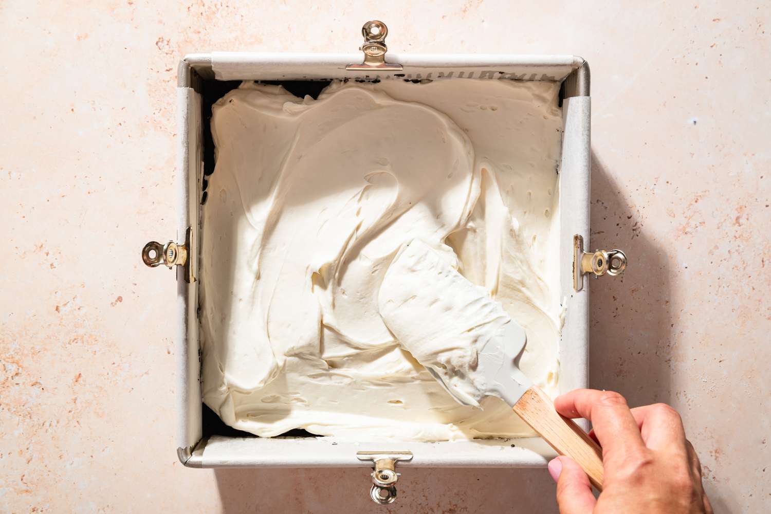 Overhead view of the cream cheese mixture being spread over the chilled crust in a pan for Chocolate Delight recipe