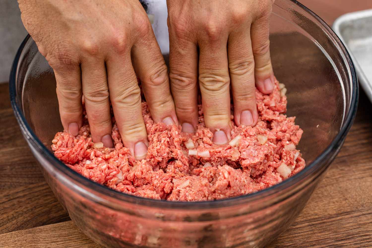 Using hands to mix in ingredients to make a classic bacon cheeseburger