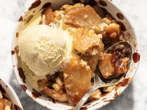 Closeup view of a serving of caramel apple cobbler topped with a scoop of vanilla ice cream in a bowl