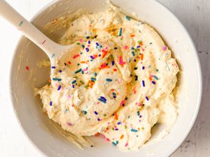 A bowl of yogurt frosting topped with sprinkles, stirred with a spoon