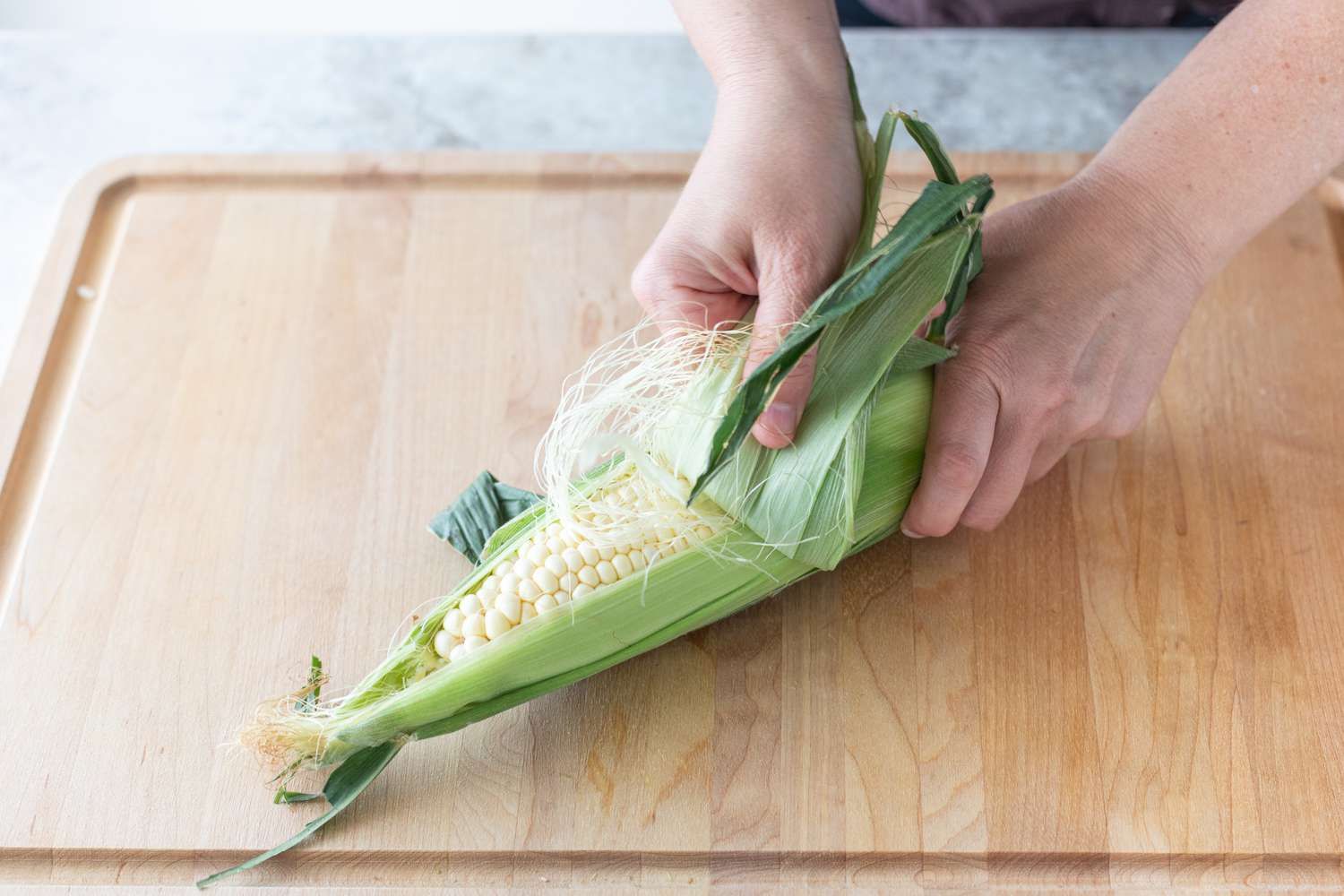 Hand shucking an ear of corn
