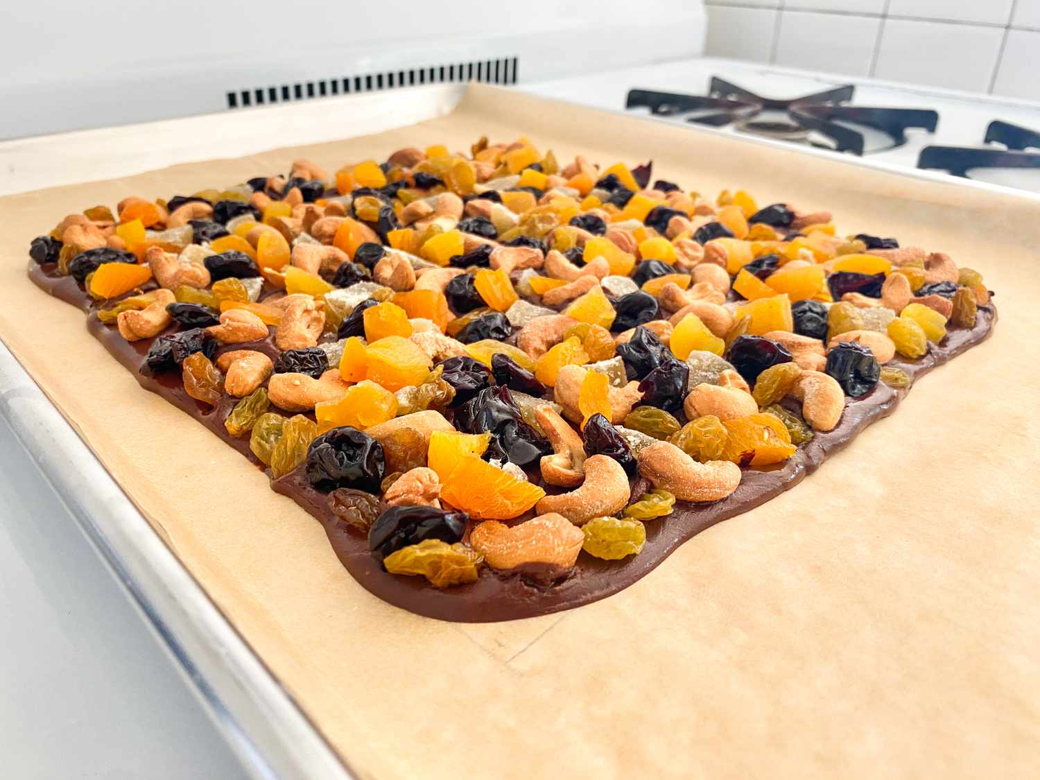 Close-up of chocolate bark on a sheet pan showing it topped with golden raisins, dried apricots, dried cherries, and cashews