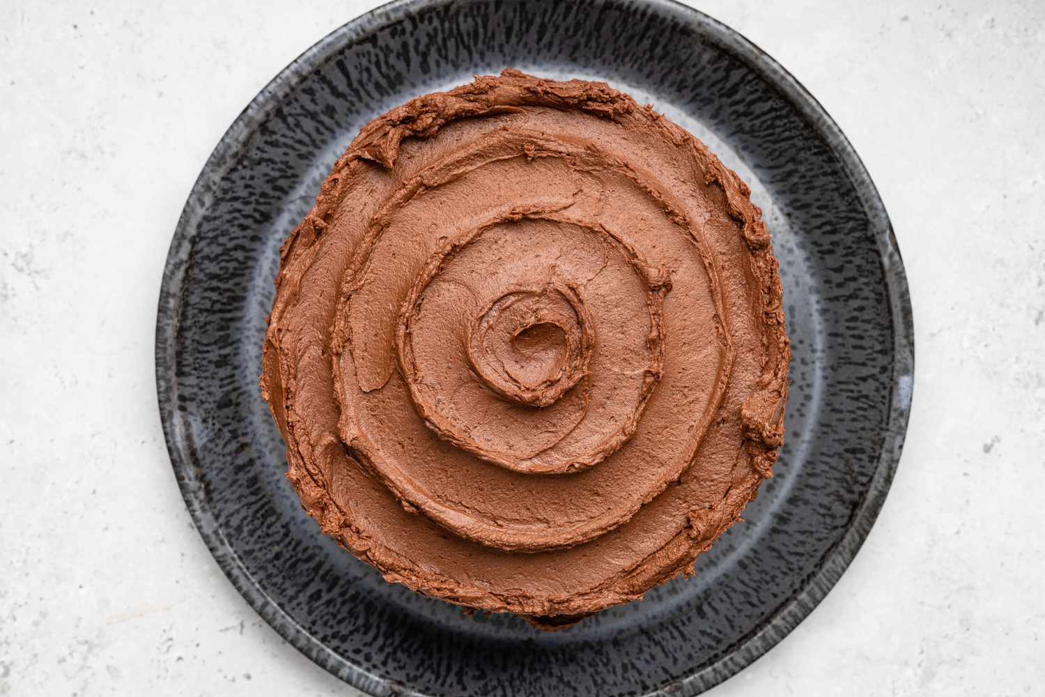 Top of One-Bowl Double-Layer Chocolate Cake Decorated With a Large Swirl and Parchment Paper Removed from Plate