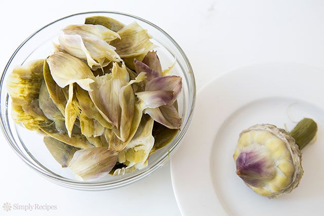 A bowl of artichoke discarded leaves and the cooked heart on its own plate to the side