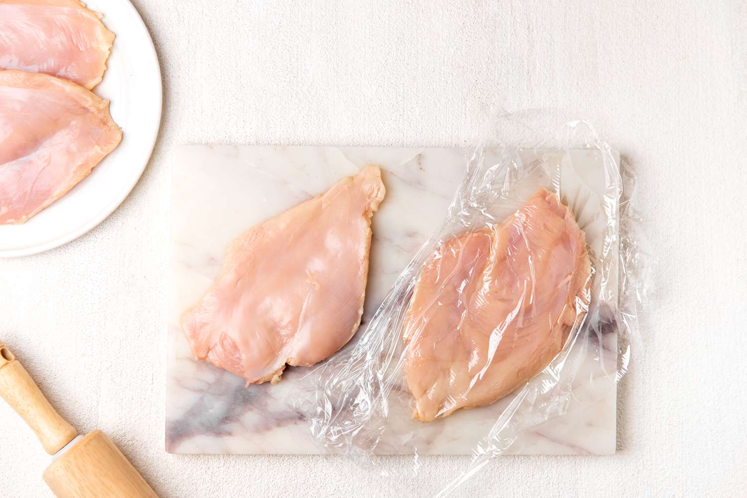 chicken breast flattened under a piece of plastic wrap for Italian butter chicken (petti di pollo al burro) recipe