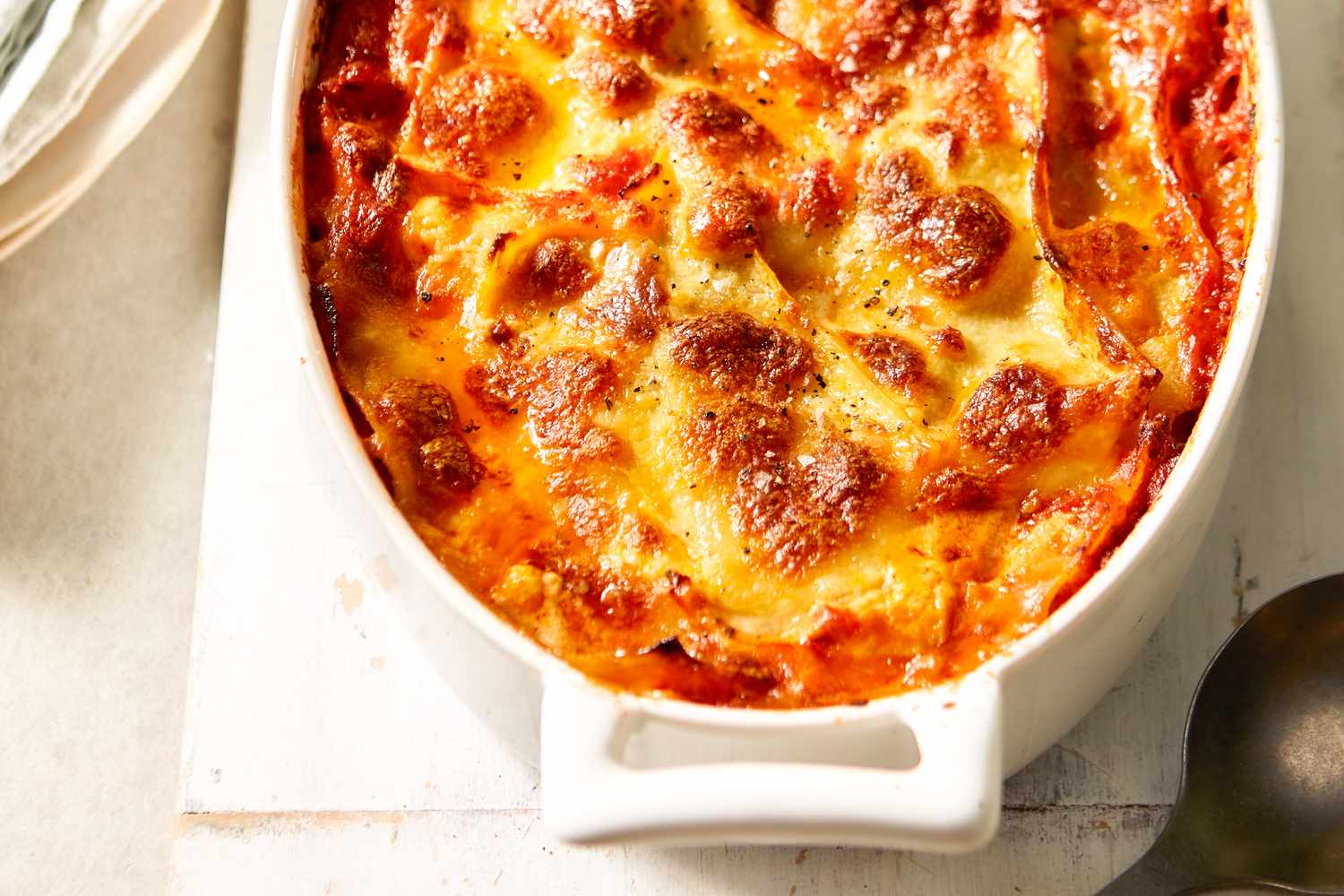A freshly baked lasagna with melted cheese in a white casserole dish zoomed in on top of a light background