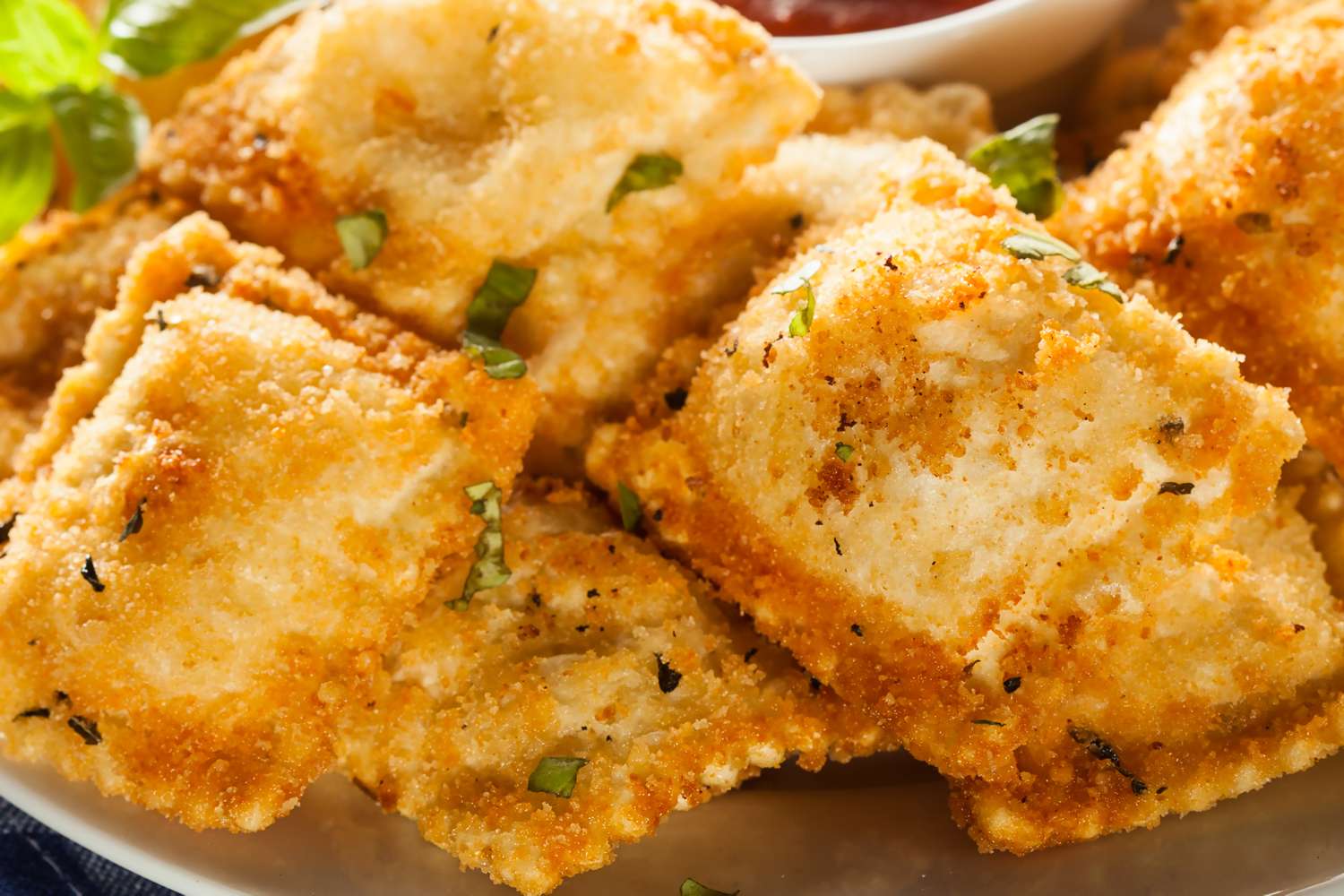 Crispy airfried ravioli on a plate garnished with herbs a bowl of dipping sauce in the background