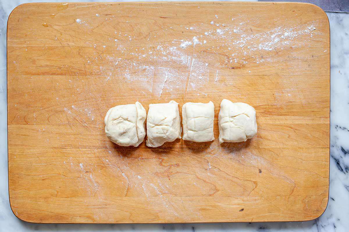 Four equal pieces of dough are on a cutting board for a flour tortilla recipe.