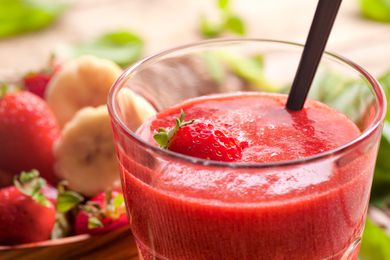 A strawberry smoothie in a glass with a straw and fresh strawberries around
