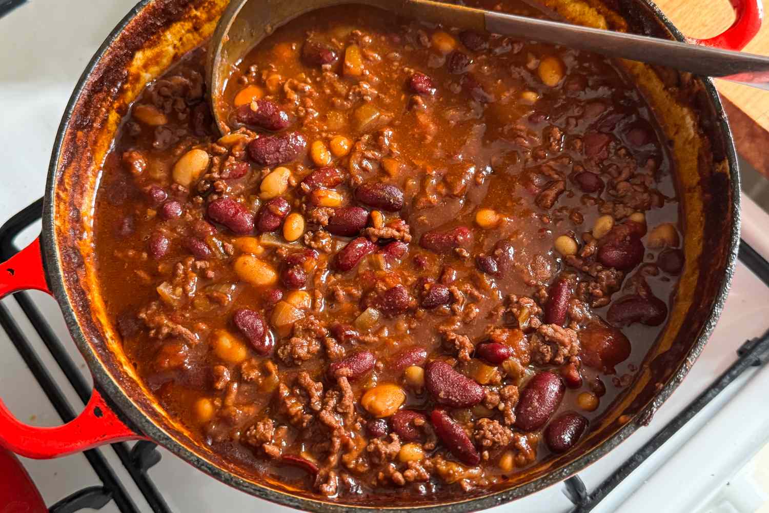 A pot of chili with ground meat beans and spices being stirred with a ladle