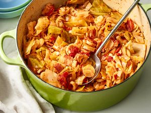 Angled view of a green dutch oven of swamp cabbage with a metal serving spoon