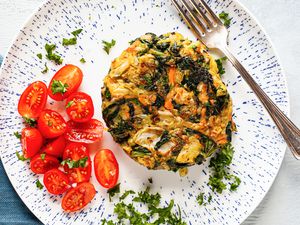 Plate of Bubble and Squeak Topped with Herbs and Side of Halved Cherry Tomatoes with a Fork