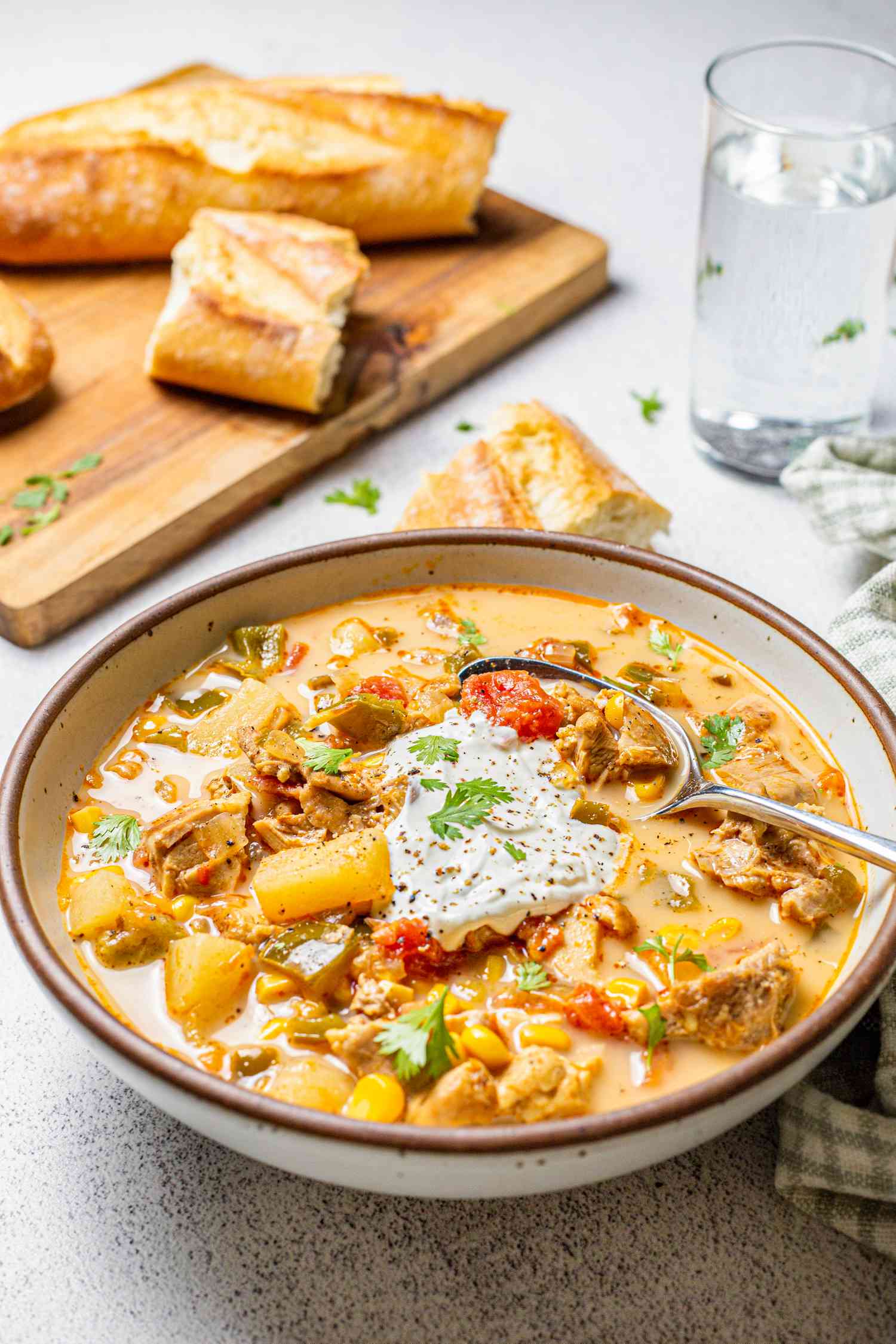 Bowl of Chipotle Chicken Chowder with a Wooden Board with Baguette Pieces in the Background