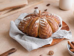 Pumpkin-shaped sourdough on a grey linen with cinnamon sticks next to it.