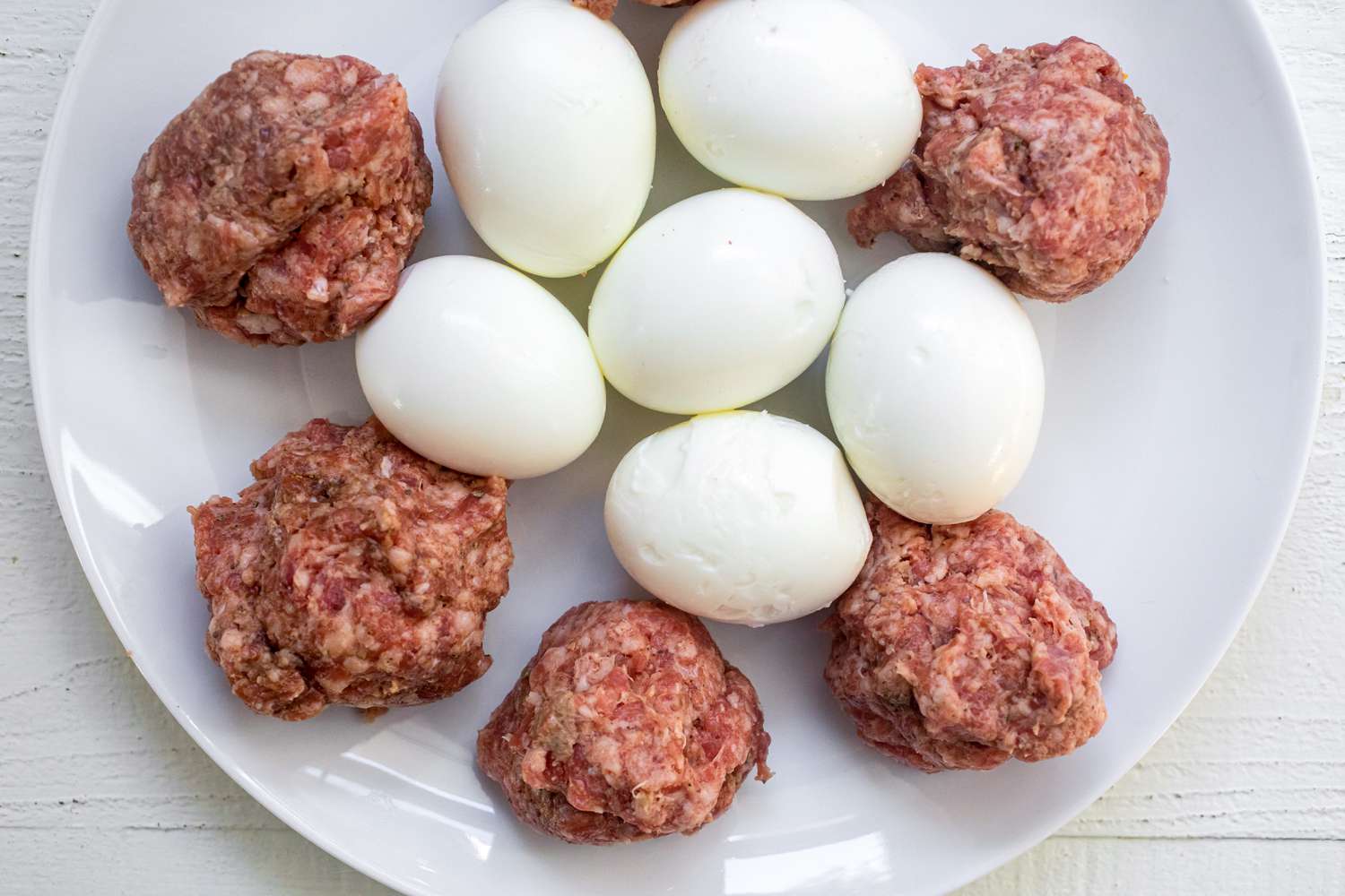 Sausage mixture with peeled eggs on a white plate. 