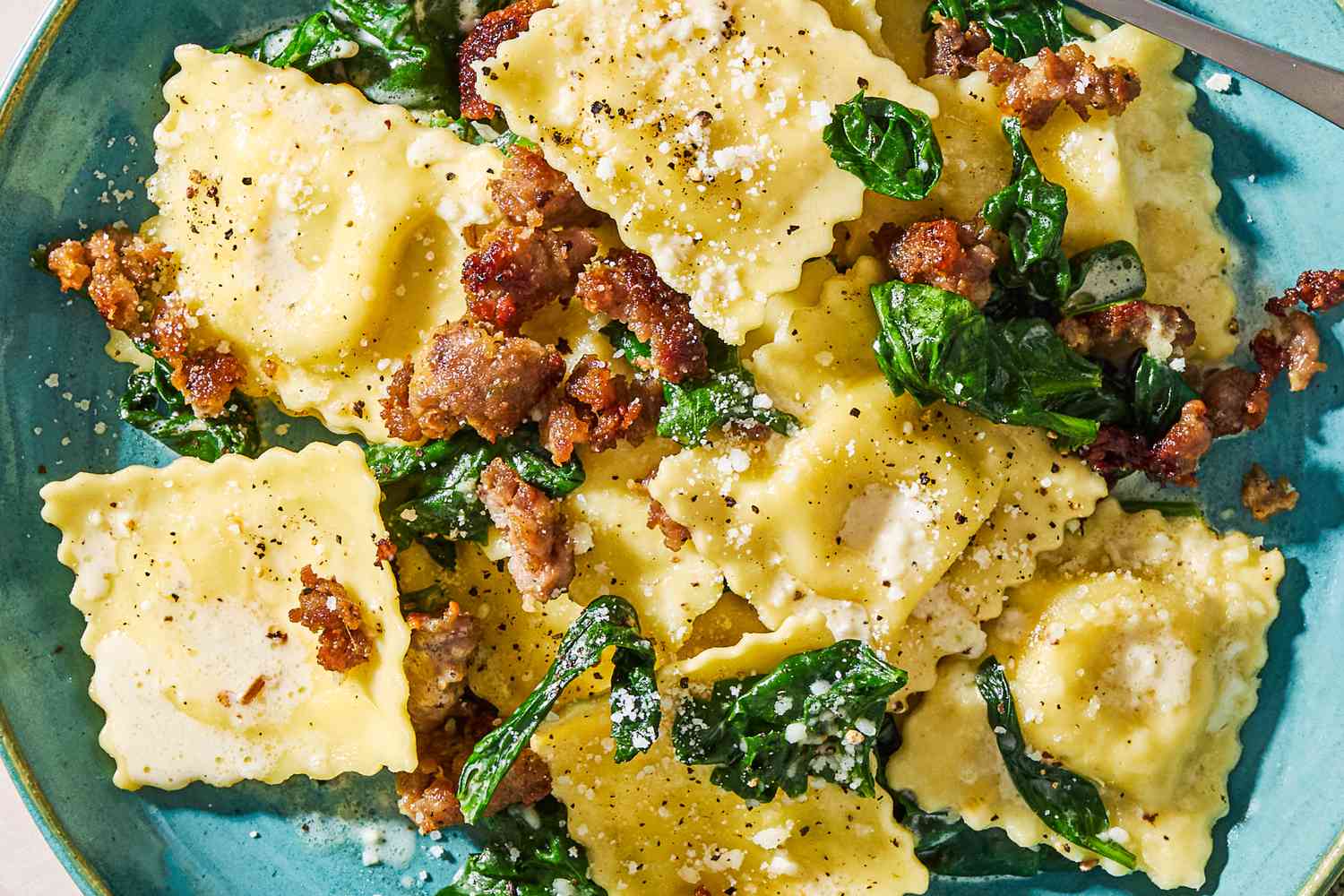 Closeup view of ravioli, Italian sausage and spinach topped with Parmesan cheese in a light blue bowl