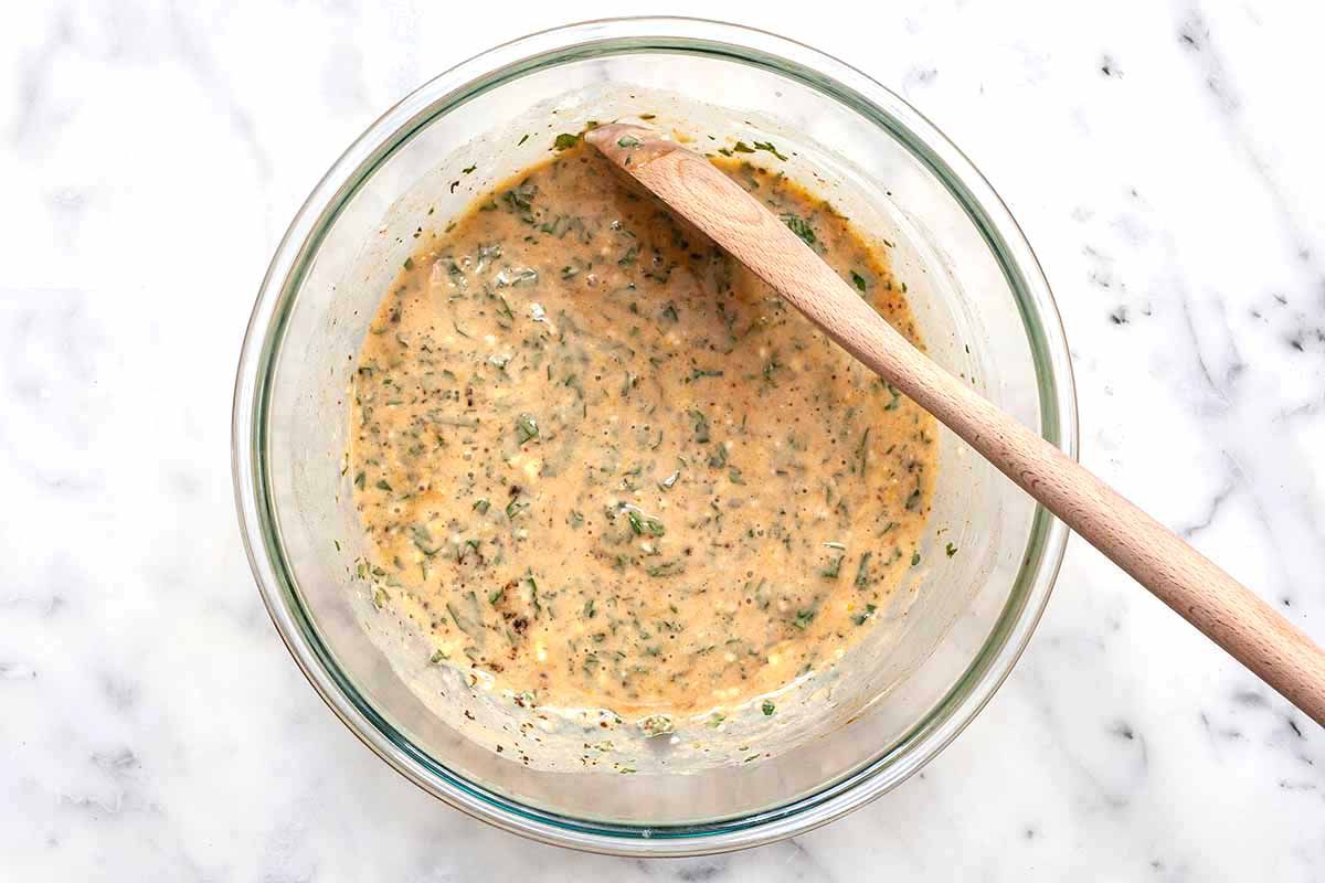 A bowl of easy homemade crabcakes with spices, mayo and breadcrumbs in a glass bowl with a spoon.