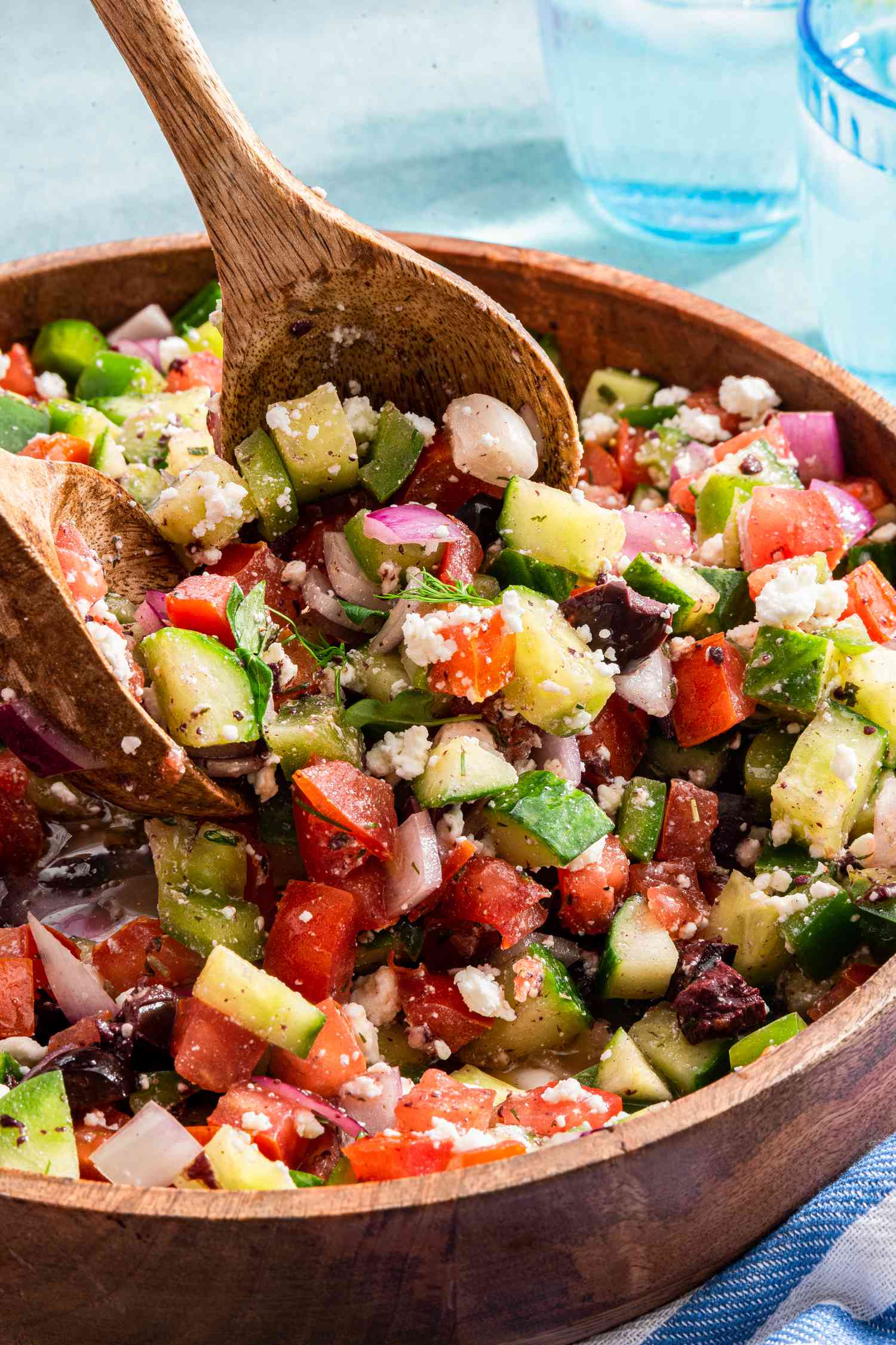 Serving Utensils Lifting Some Easy Greek Salad From the Bowl, and in the Background, Two Glasses of Water 