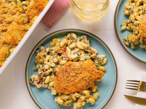 Overhead view of chicken and pasta casserole serving on a blue plate next to a dish of casserole, table napkin and drinking glass with ice and beverage
