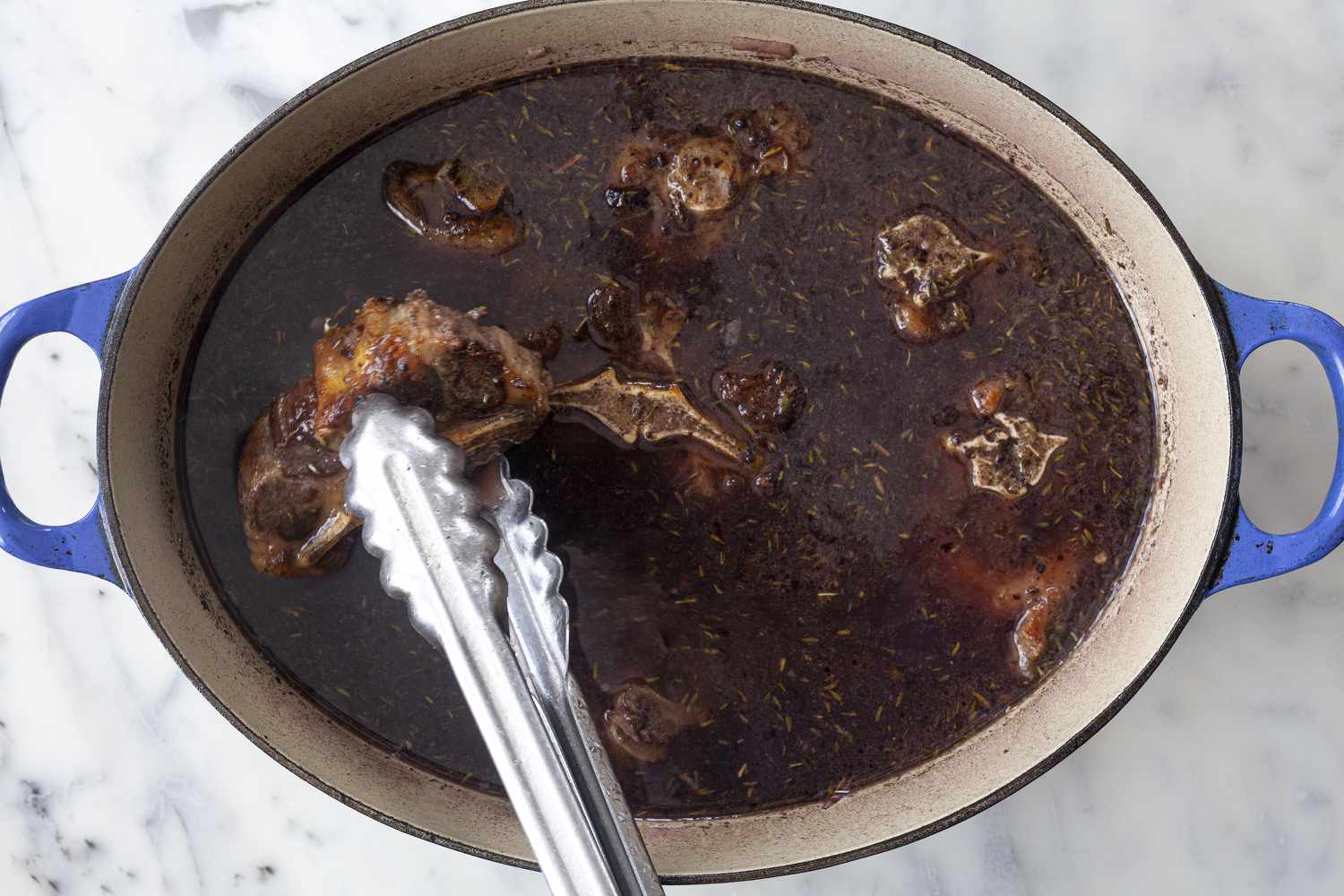 Oxtails added to the braising liquid in a dutch oven to show how to cook oxtails.