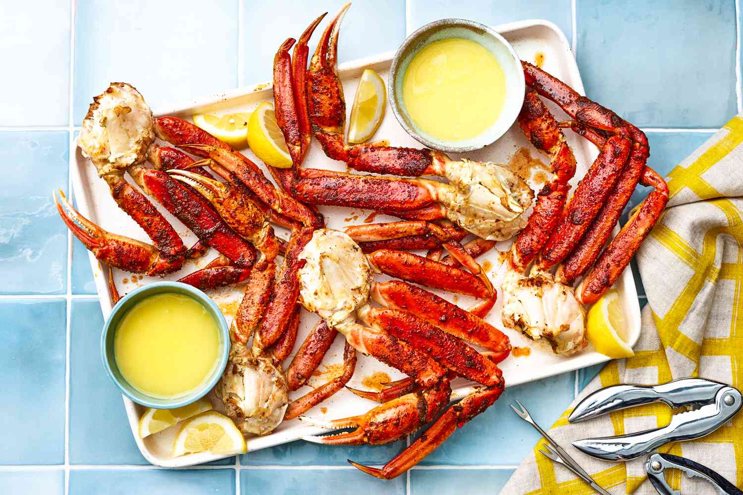 Tray of Easy Baked King Crab Legs With Bowls of Melted Butter and Lemon Wedges, and on the Counter Next to It, a Few Seafood Picks and Cracker on a Table Napkin