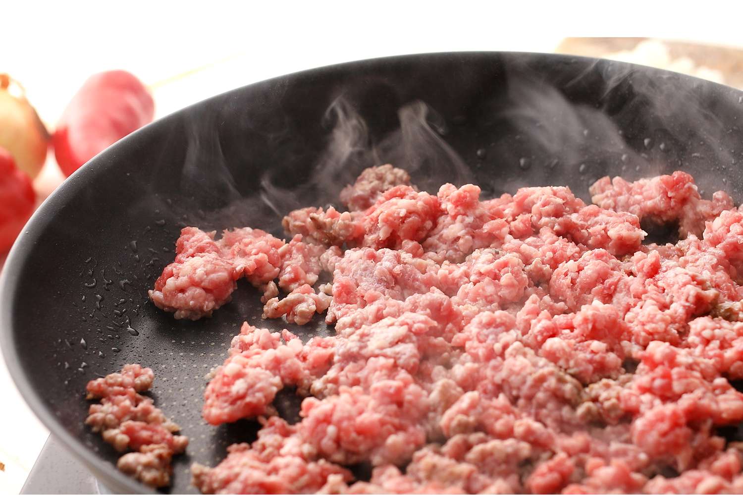 Ground beef cooking in a frying pan emitting steam