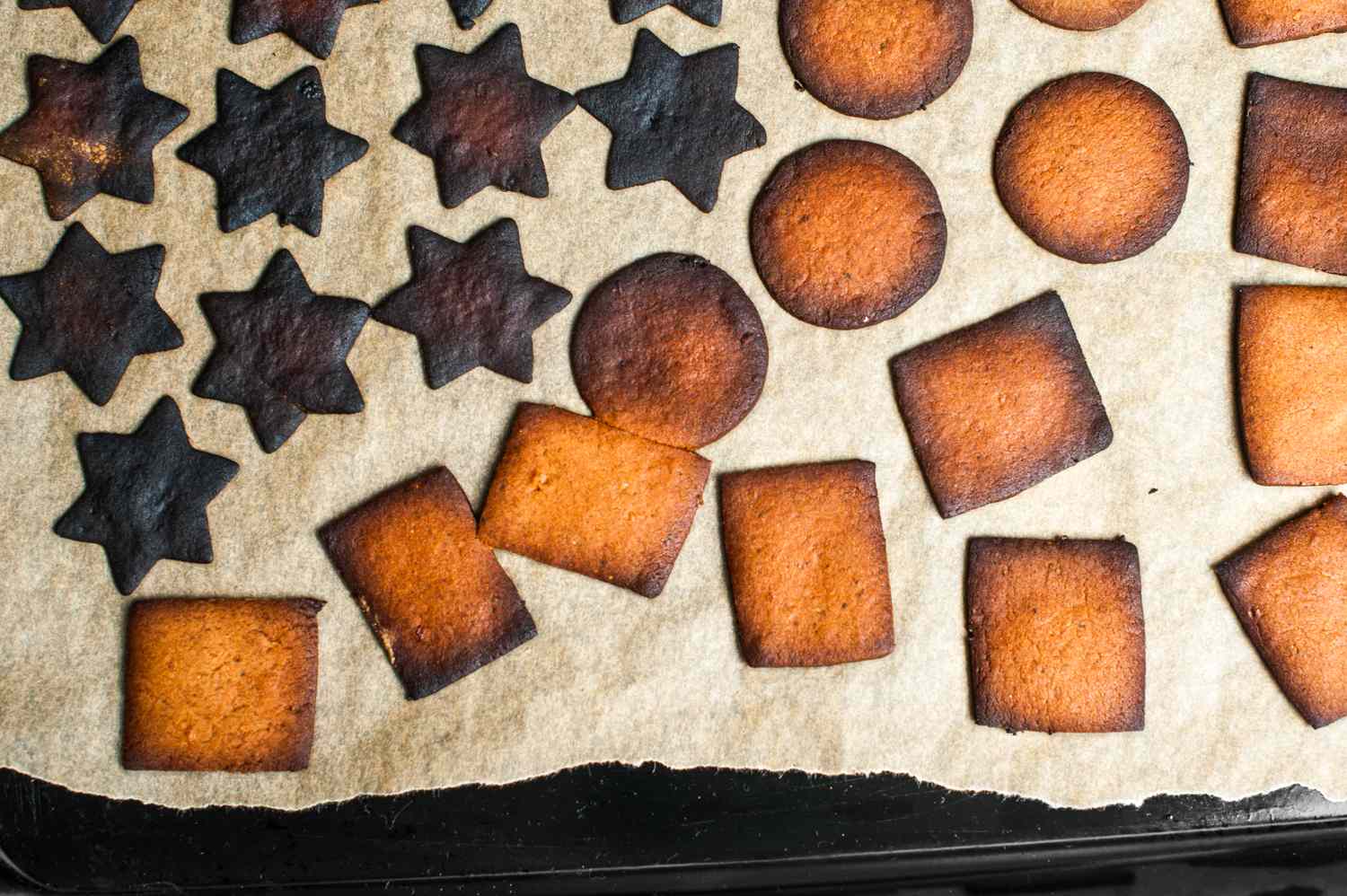 A baking sheet with overcooked cookies of various shapes on parchment paper