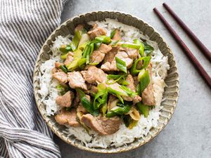 Pork stir-fry with green onions served on rice in a bowl, chopsticks on the side