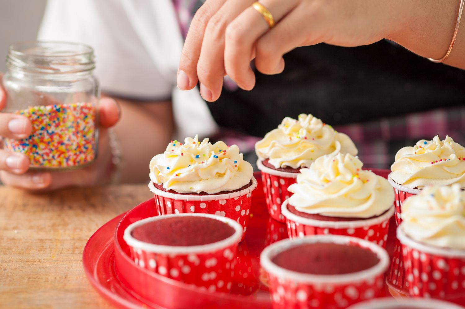 Someone adding sprinkles to cupcakes