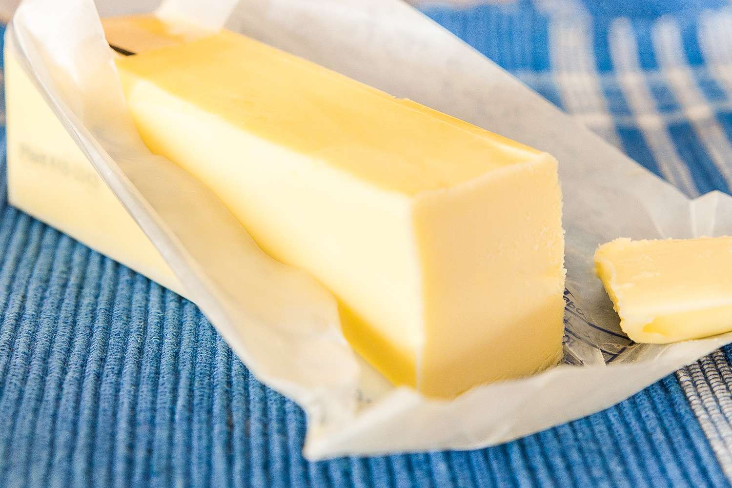 A stick of butter partially unwrapped on a blue surface