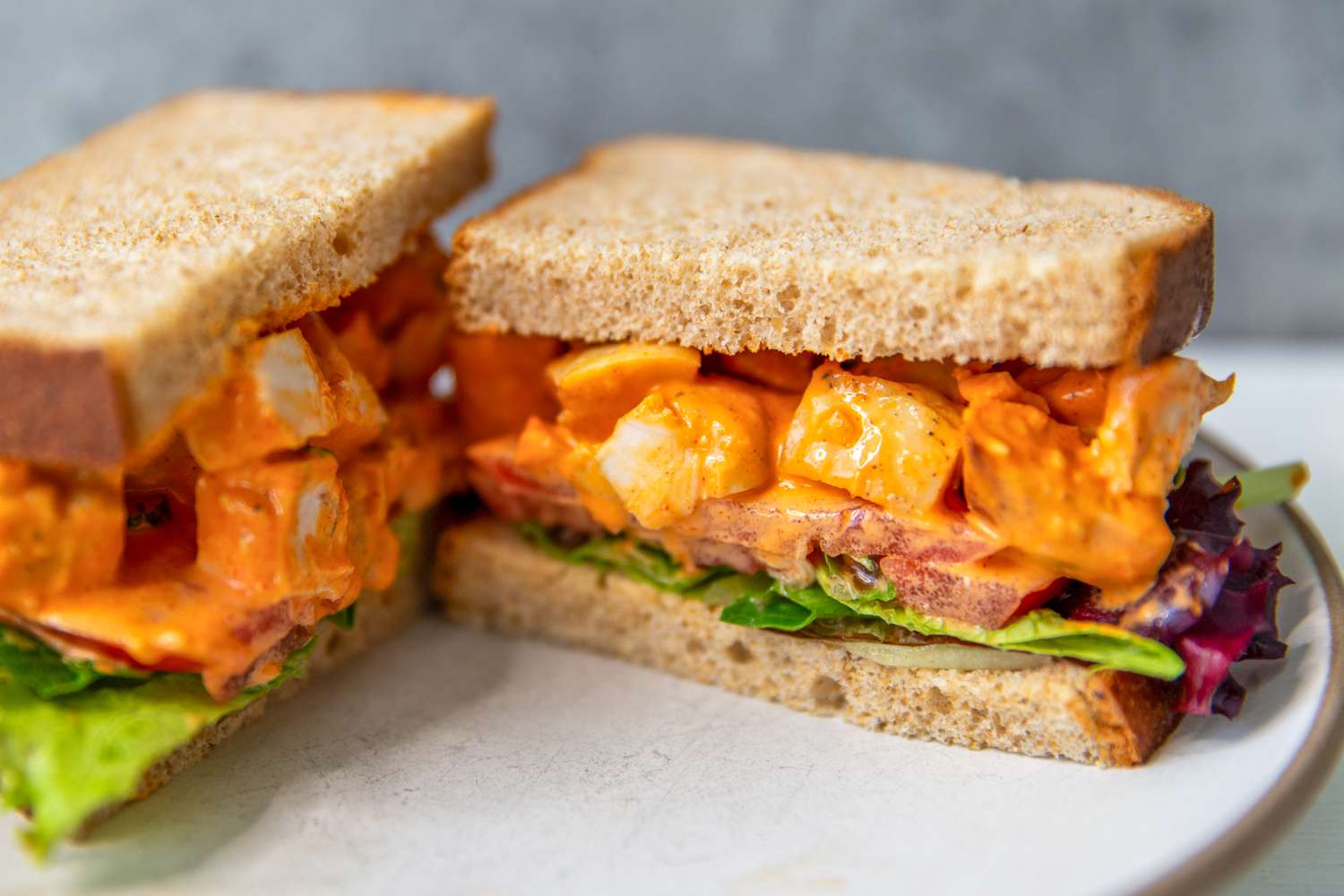 Sideview of a gochujan chicken salad sandwich on toast split in half on a plate