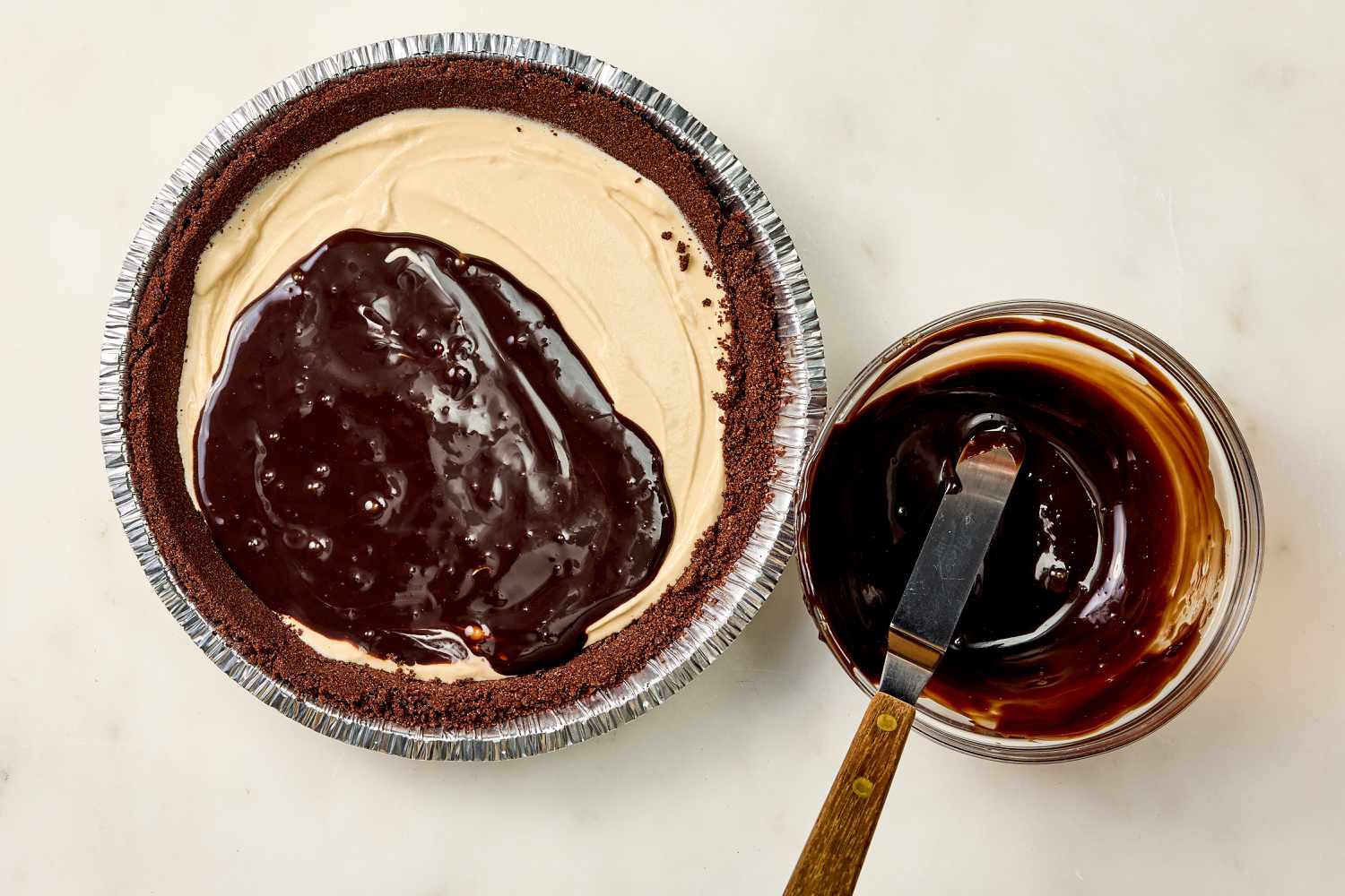 overhead view of chocolate cookie pie shell filled with ice cream mixture, being topped with hot fudge