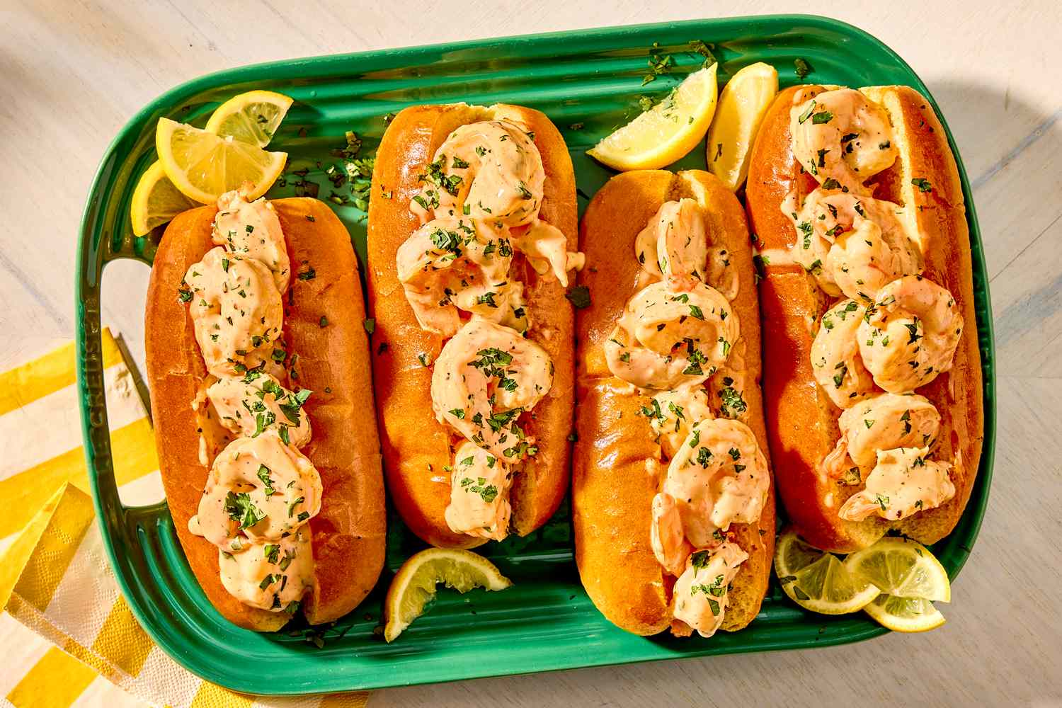 Four shrimp rolls on a green platter with lemon wedges and garnishes