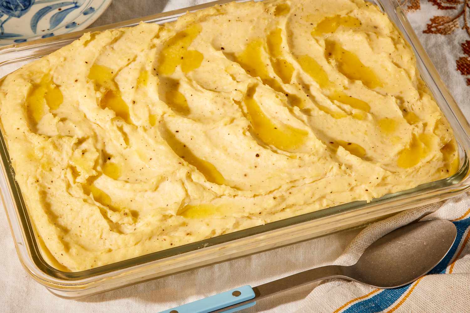 Angled view of a clear glass baking dish of almond milk mashed potatoes topped with butter