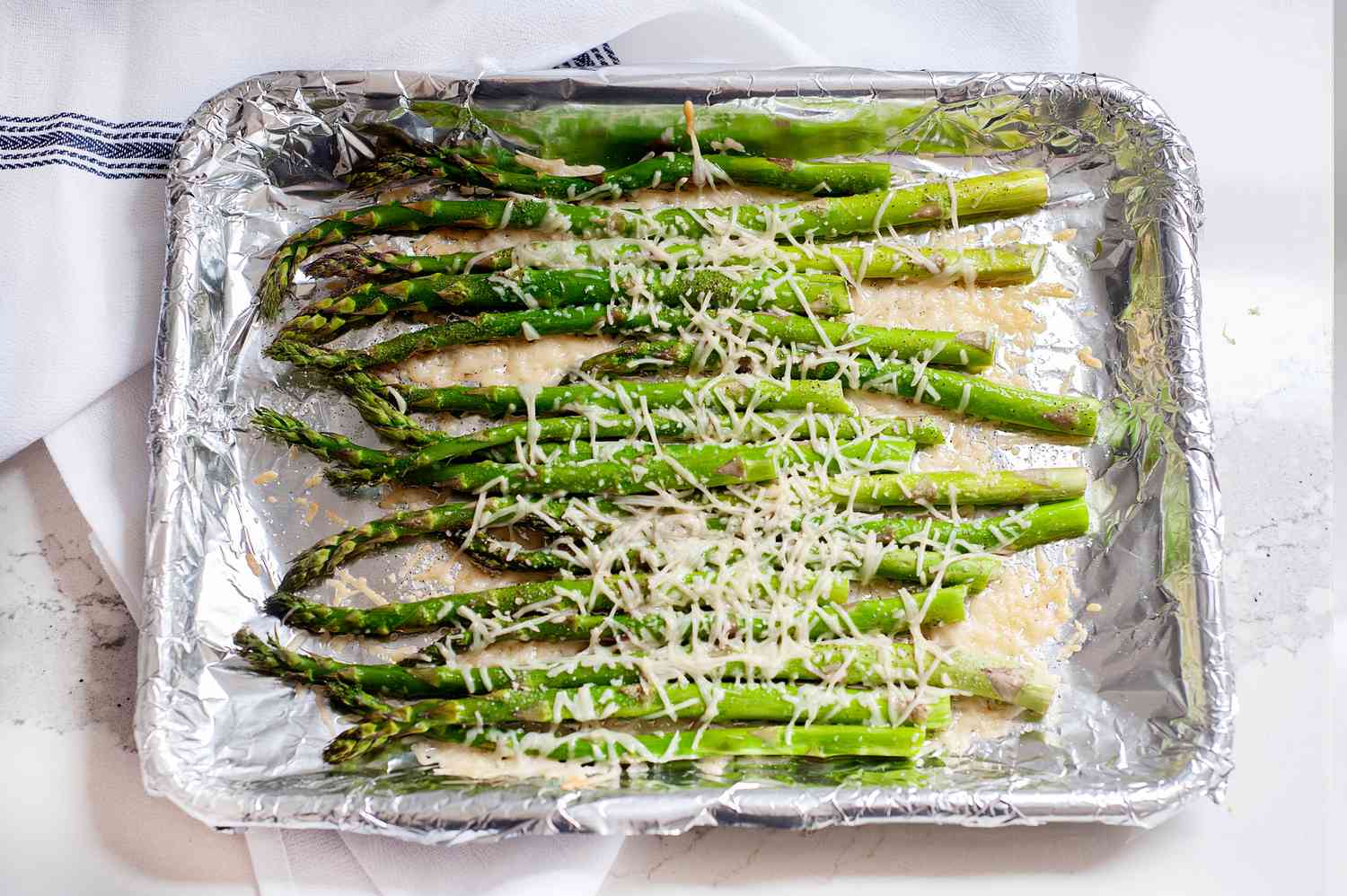 A baking tray with baked asparagus topped with parmesan