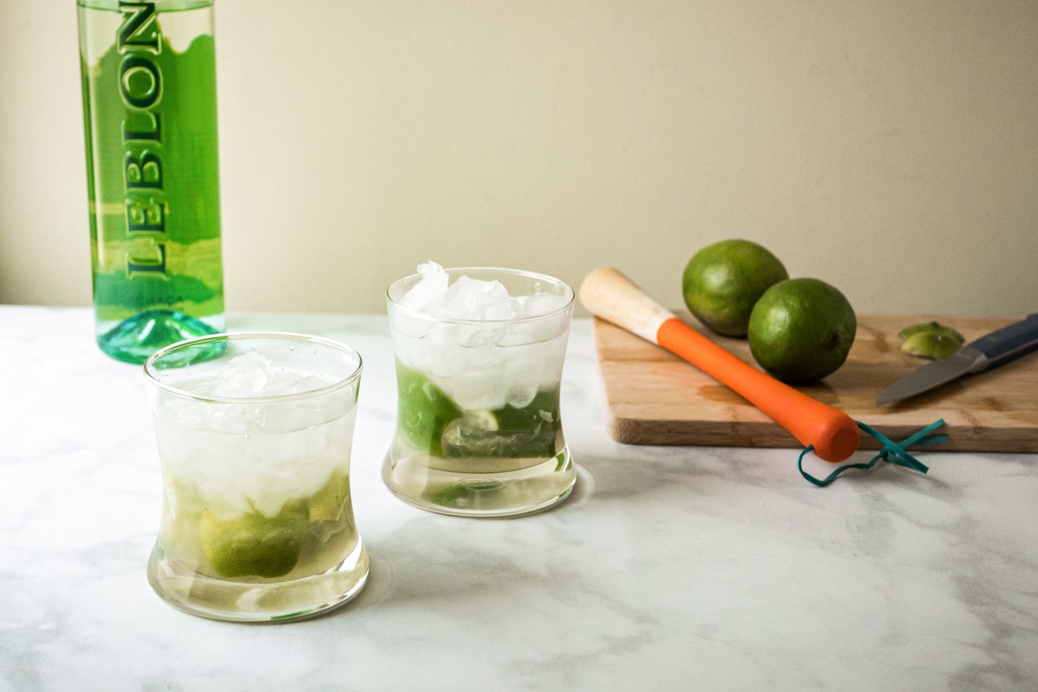 Two Brazilian caipirinha cocktails and a cutting board with limes and a muddler.