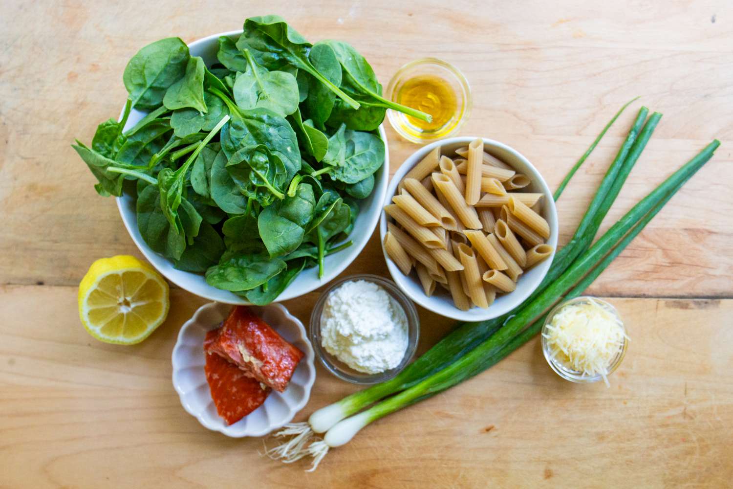 Ingredients for a pasta dish including spinach pasta smoked salmon ricotta cheese green onions grated cheese olive oil and a lemon slice