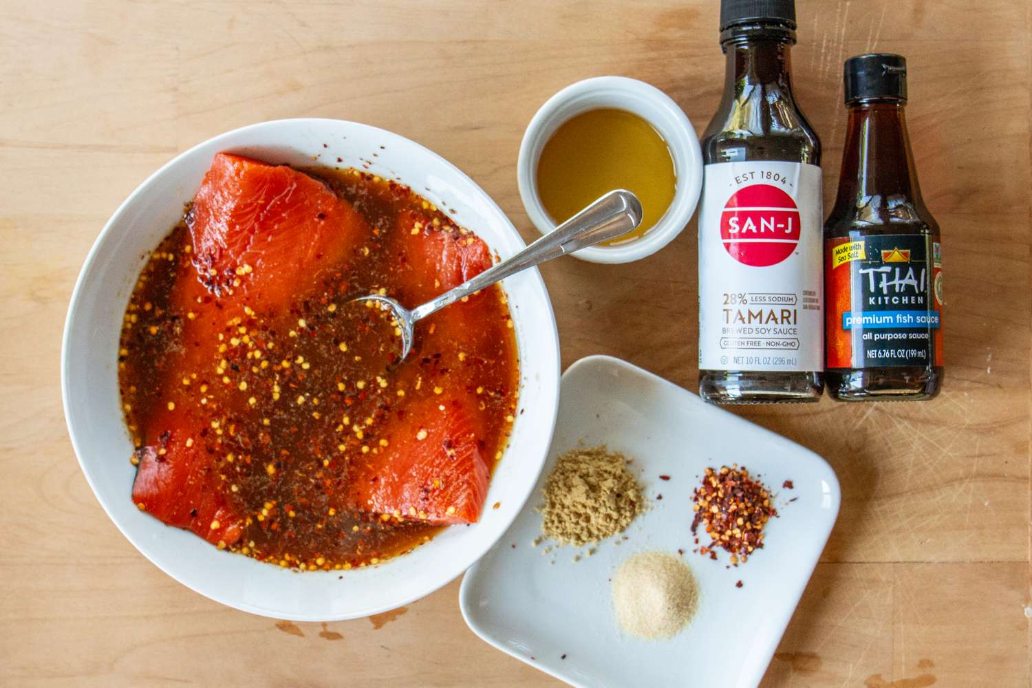 A preparation of salmon marinating in a sauce with spices and seasoning, alongside bottles of soy sauce and oil