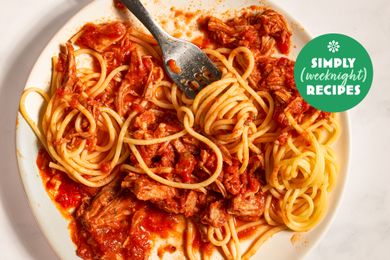 A plate of spaghetti with a meat and tomato sauce partially eaten and a fork placed on top