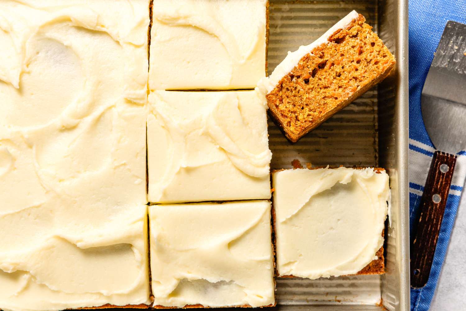 Sliced frosted carrot cake in a baking pan with one raised piece
