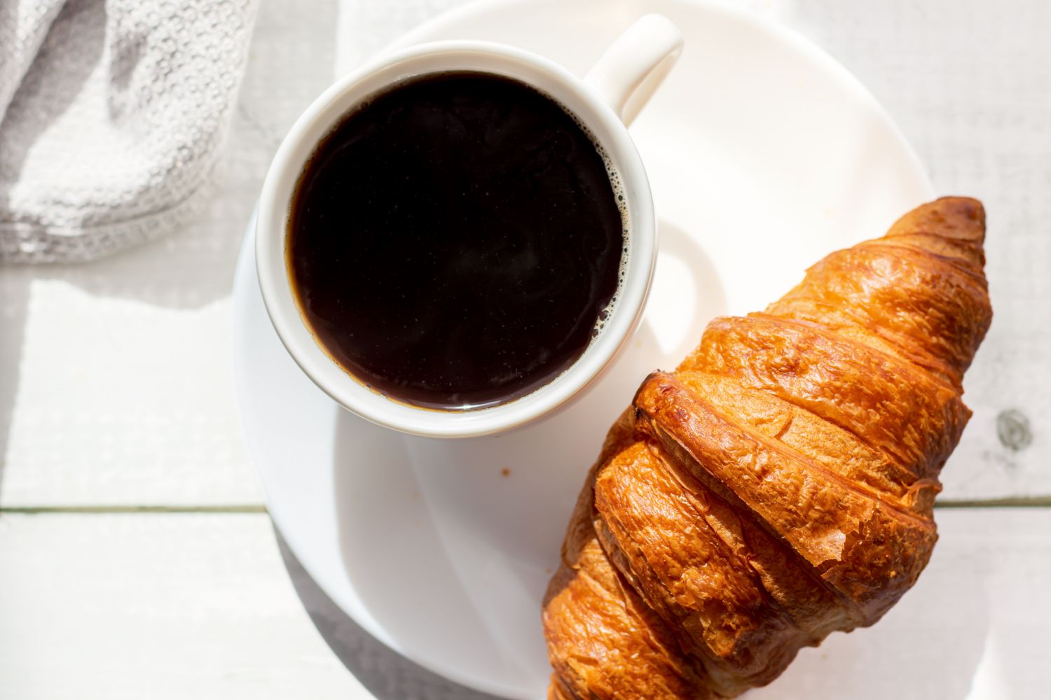 A cup of coffee and a croissant served on a white plate