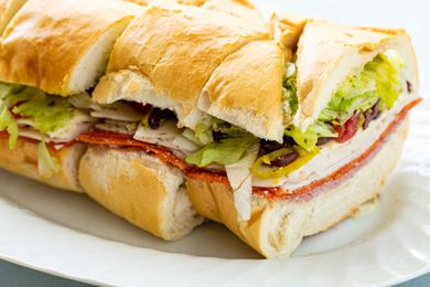 Side view of an italian sandwich on a platter that is cut into slices. Meat, cheese and toppings are layered on the sandwich.