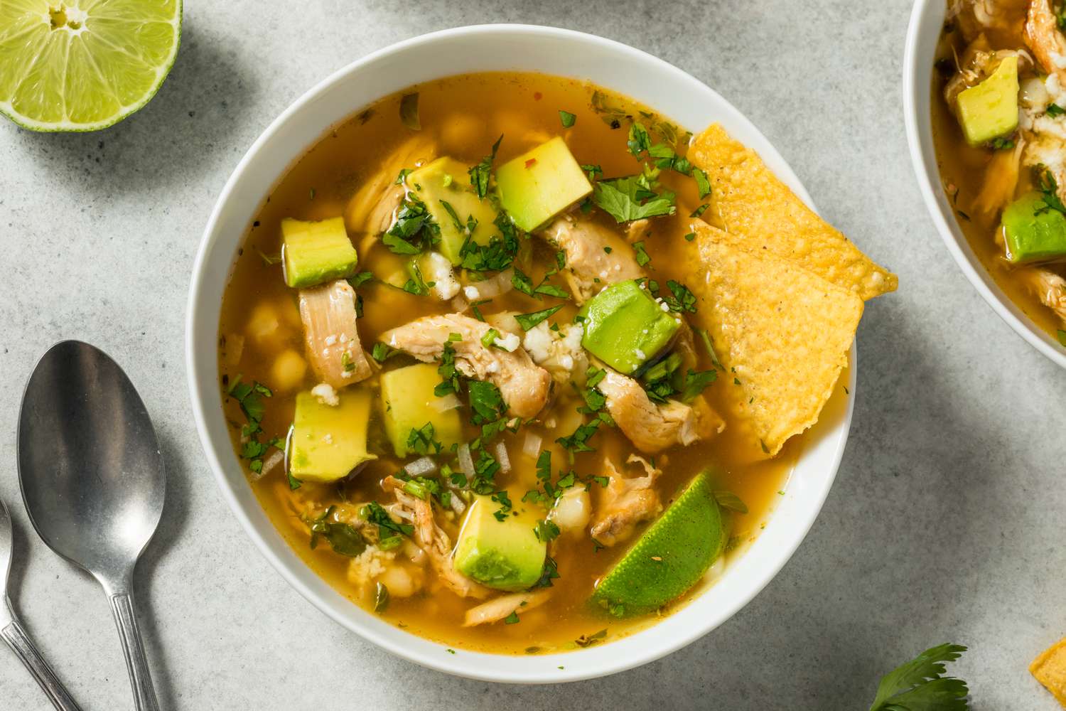 Bowl of posole with avocado tortilla chips and lime