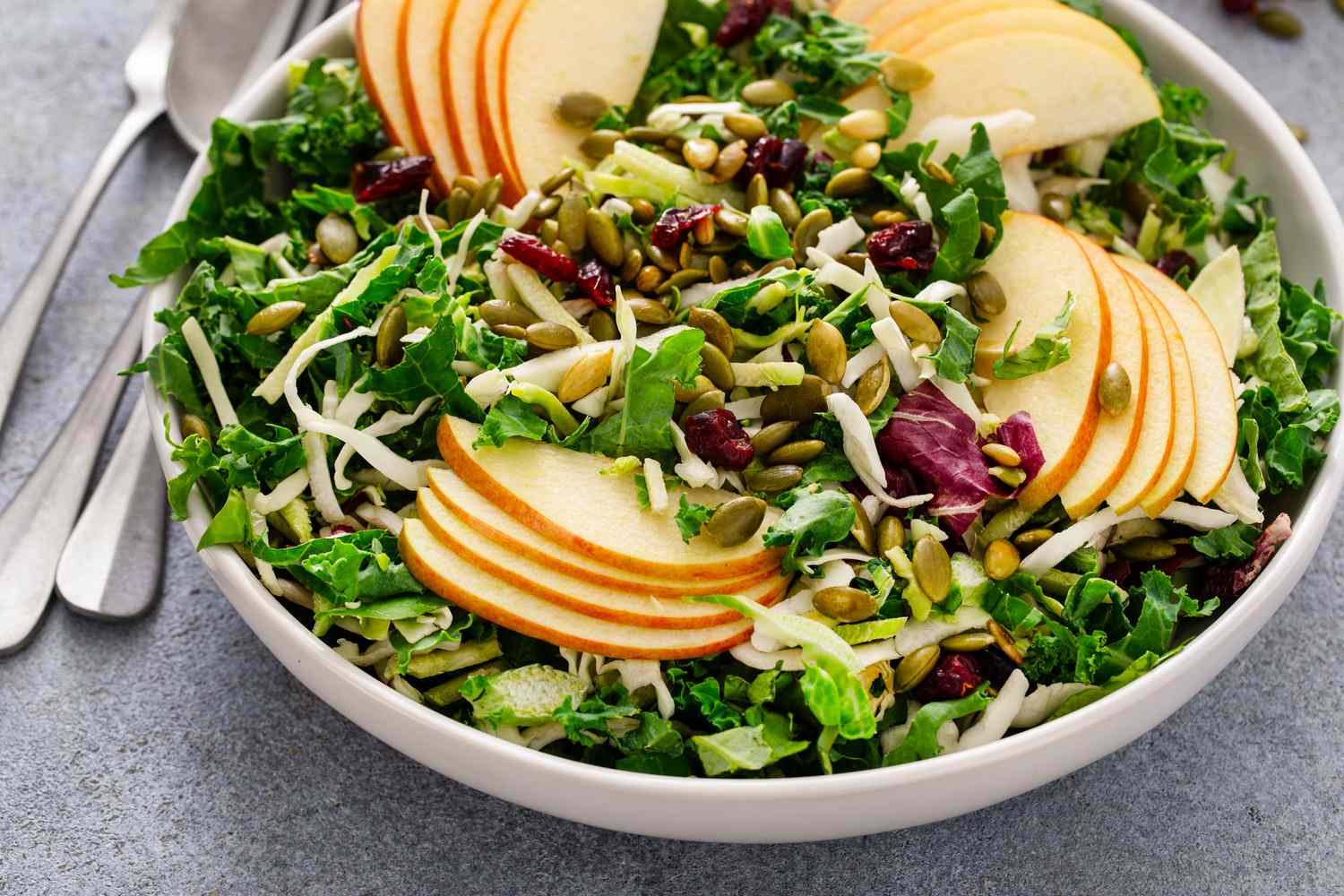 Fall salad with kale, cabbage, and apples, topped with pumpkin seeds and dried cranberries